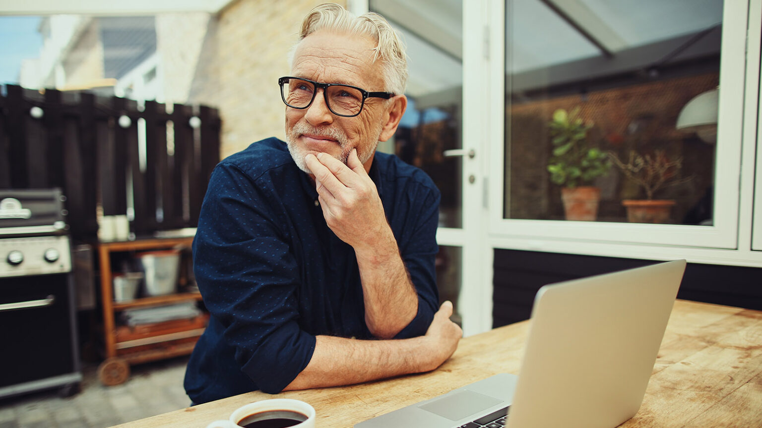 Senior Man Sitting Outside Drinking Coffee And Using A Laptop