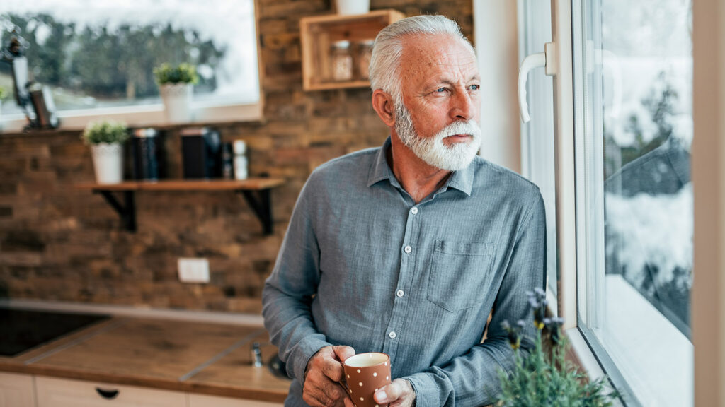 Senior Man Drinking Coffee And Looking Through Window, At Home.